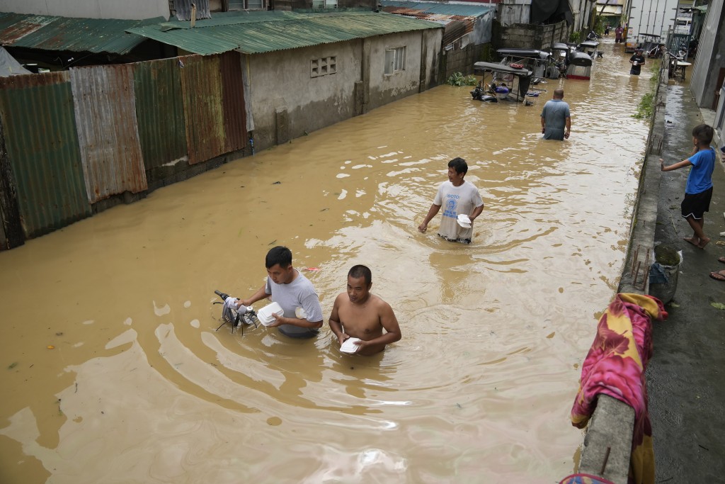 台风奥鹿吹袭下，有菲律宾市民带著食物包沿著一条被洪水淹没的街道涉水而行。AP