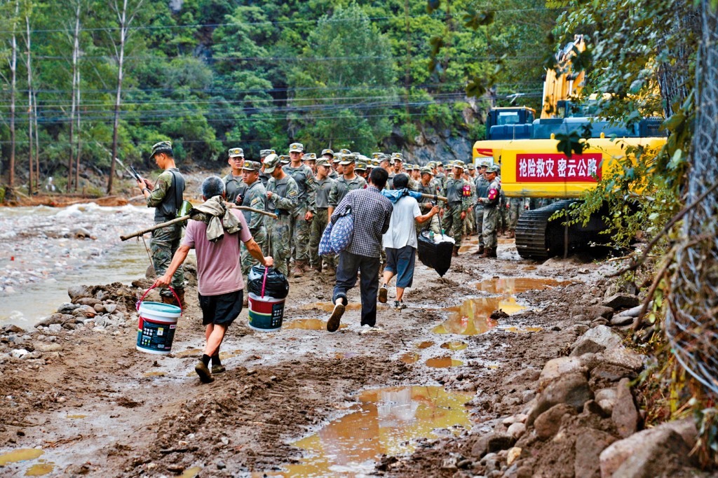 村民們攜帶個人物品，行走在被暴雨淹沒後受損的道路。