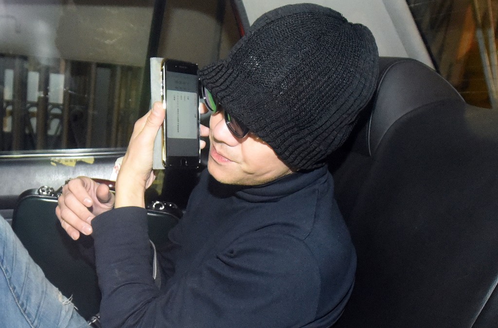 梁漢文涉嫌酒駕被捕後，電召的士離開中區警署時以手機遮面。