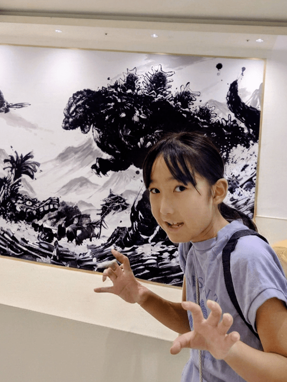 平田琉七在哥斯拉水墨壁畫前學怪獸動作，神情靈動。