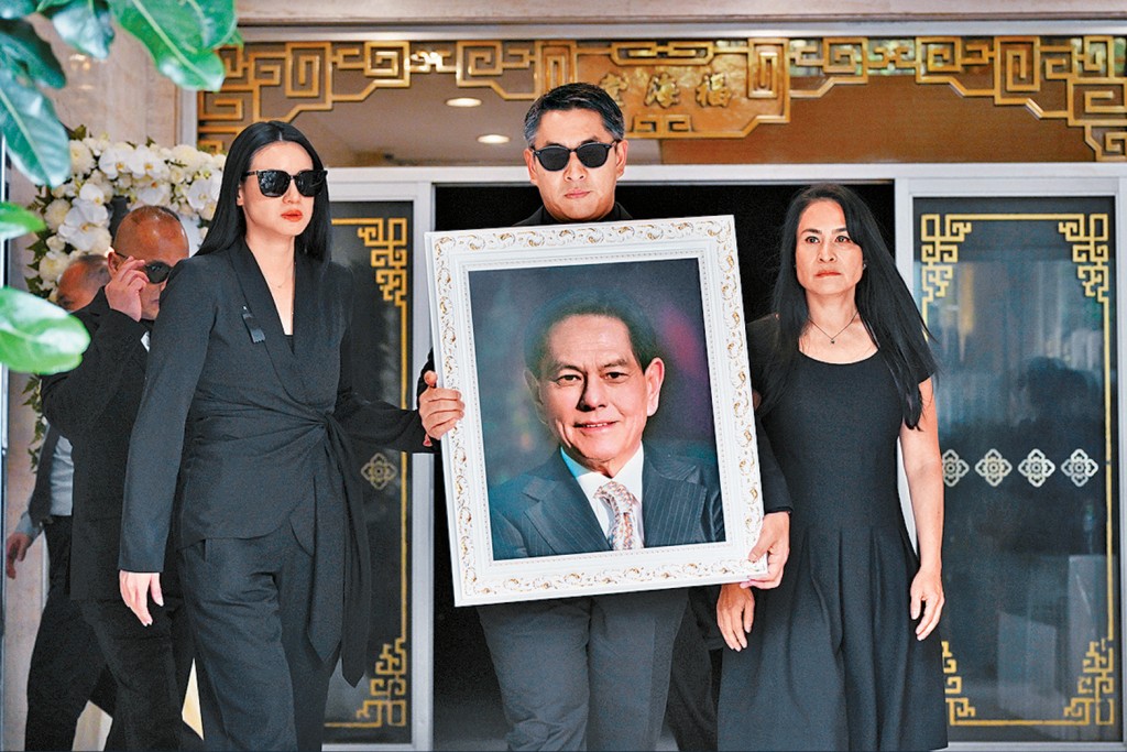 何柱國出殯,兒子何正德捧着父親遺照步出殯儀館,旁為媳婦林恬兒(左)及女兒何詩曼(右)。