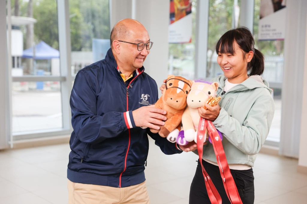 李思穎帶上三面獎牌接受《駿步人生》專訪，馬會公司事務執行總監譚志源代表馬會向她送上一對馬兒毛公仔。馬會提供