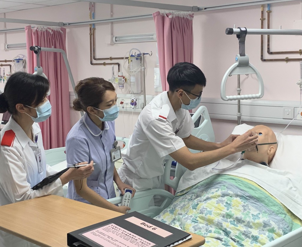 朱慧玲(左)指導袁海鑌(右)為模擬人偶戴上氧氣罩，黃子晴(中)負責調整病床角度。