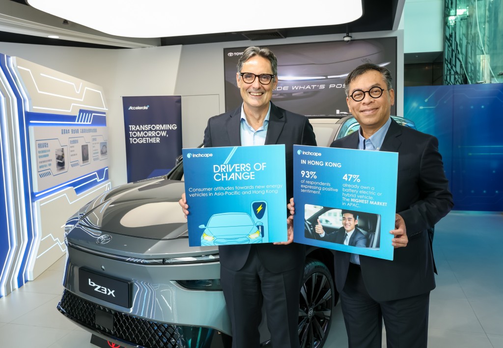 Two men in business suits hold blue informational boards in front of a Toyota bZ3X electric vehicle at an event promoting sustainable transportation and high electric vehicle adoption rates in Hong Kong.