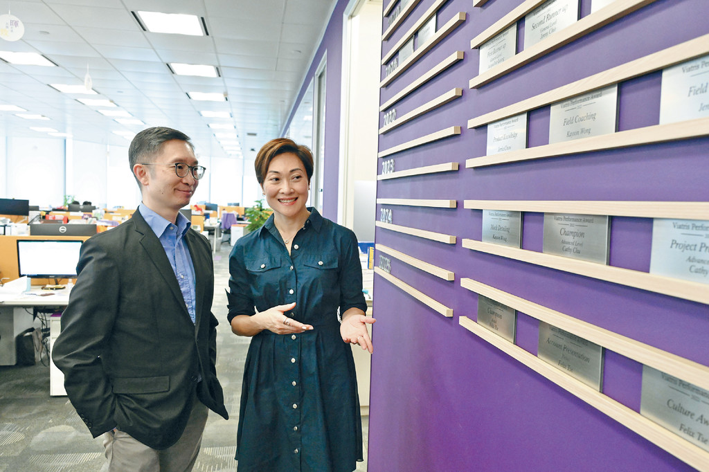 ■陳小姐向《頭條日報》廣告部副總經理劉孟輝（Jacky）展示香港總部內的出色員工展板。展板作用為鼓勵業績好或貢獻良多的員工。