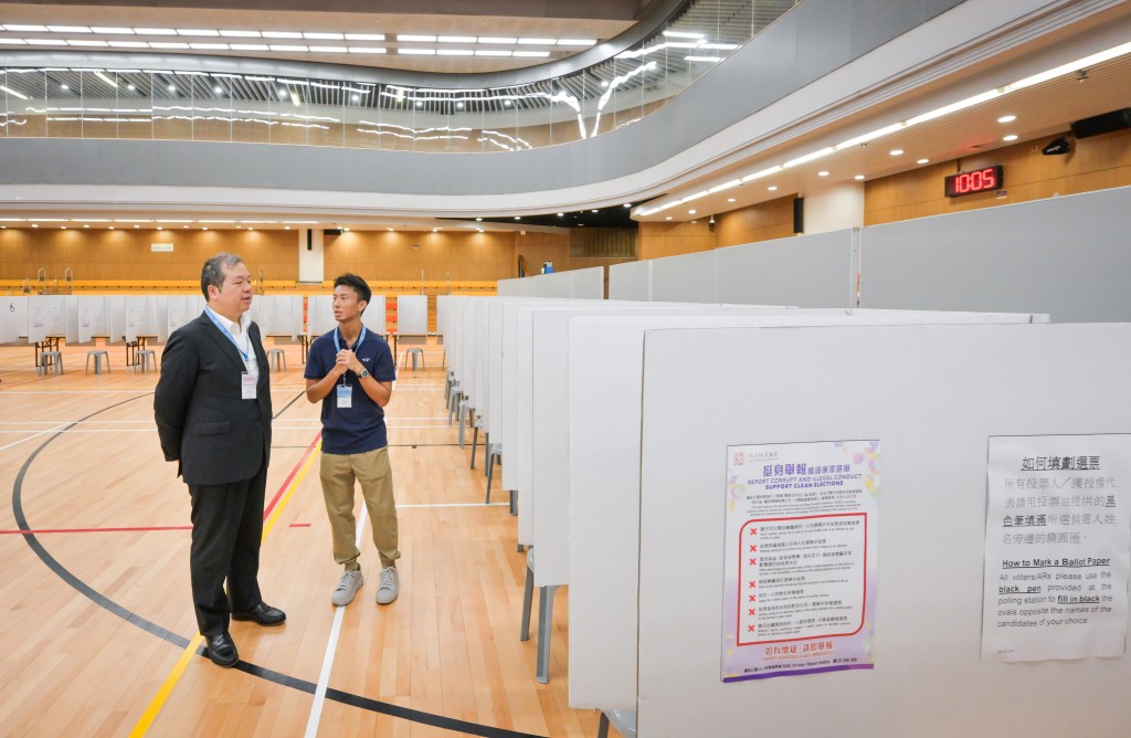文本立（左）巡視設於調景嶺體育館的2025年選舉委員會界別分組補選投票站，實地視察投票站人員的預備工作。政府新聞處