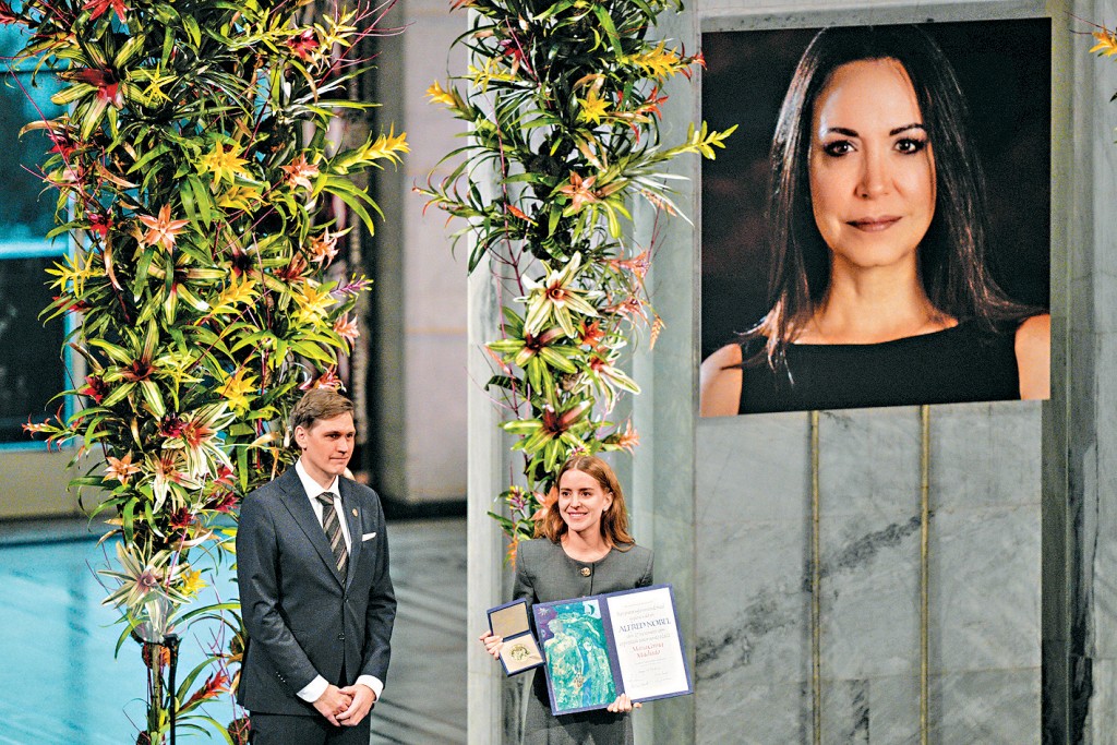 委拉瑞拉反對派領袖馬查多的女兒安娜（右）在挪威代母親取領和平獎。圖中右上角為馬查多的照片。