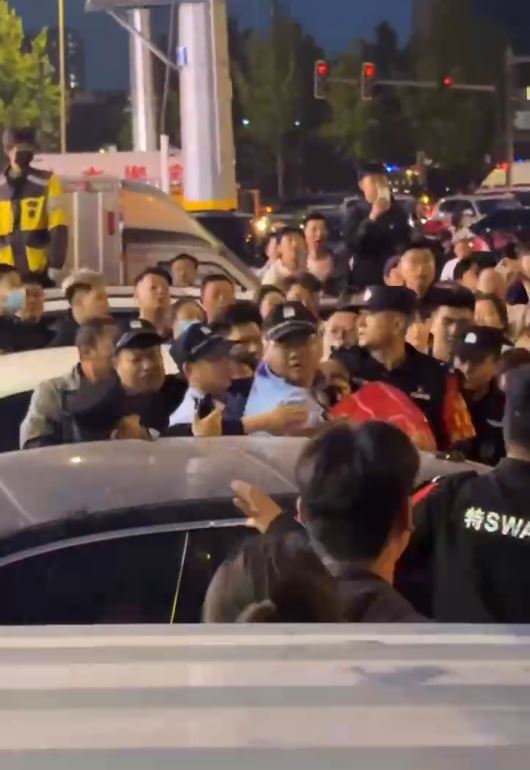 警員用身體為女事主遮擋身體，再用紅布裹身，護送她離開。影片截圖