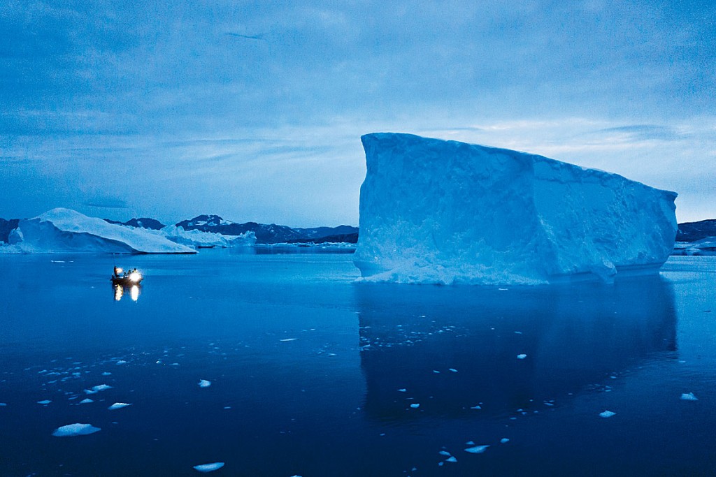一艘船在格陵蘭東部的大型冰山旁航行。 