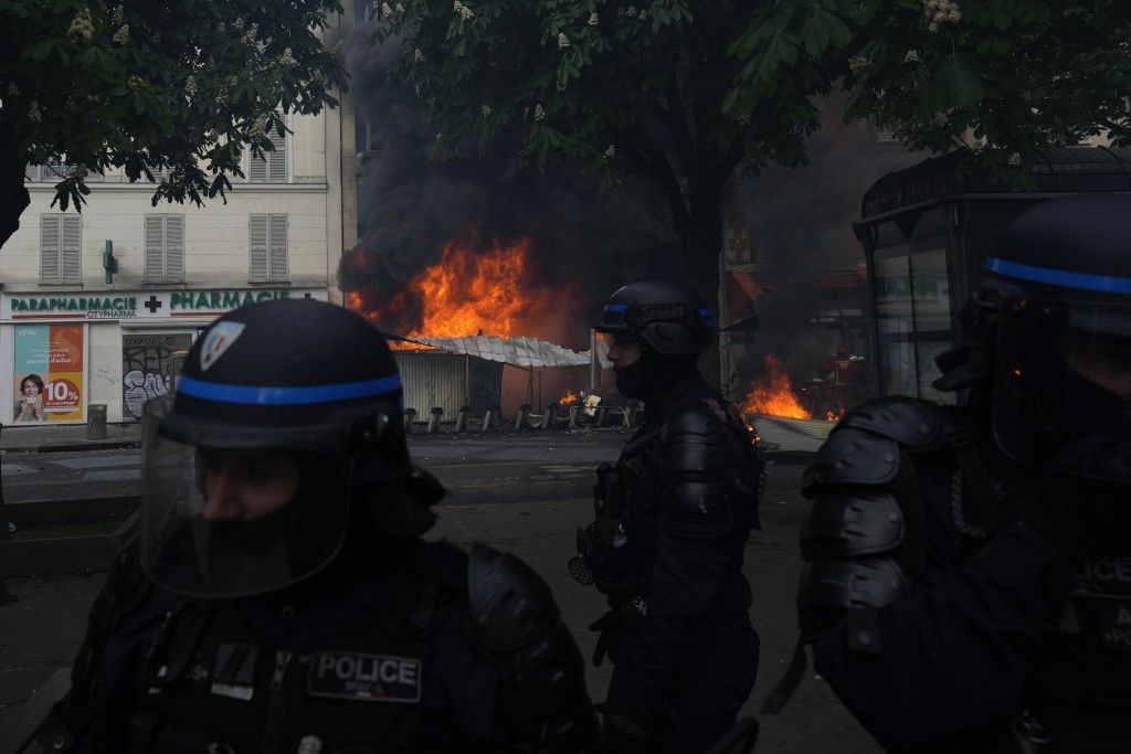 巴黎示威活动中，防暴警察站在燃烧的建筑物旁。AP
