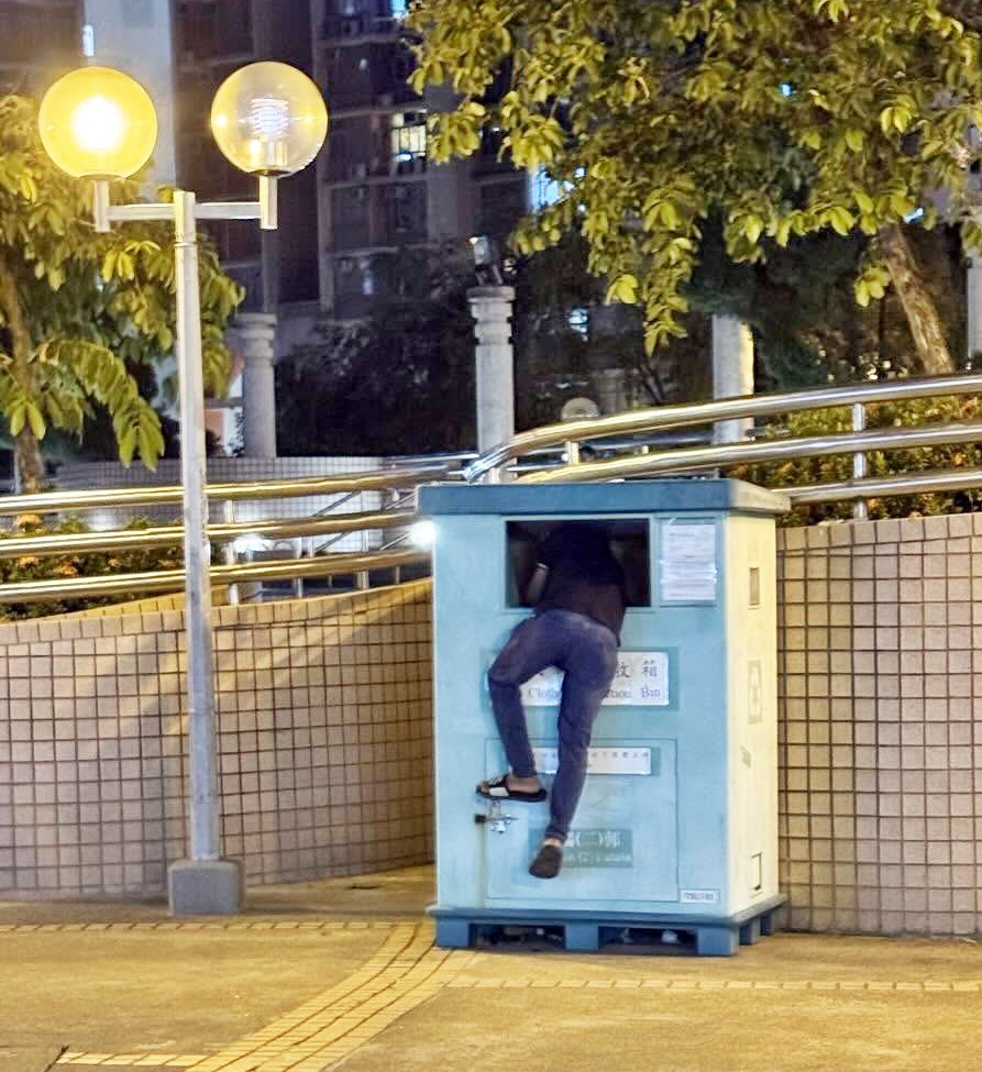 相中見到一名穿拖鞋的黑衣健碩男子， 以爬樹方式鑽入回收箱，疑似正探頭伸 手找尋箱內物品。Threads截圖