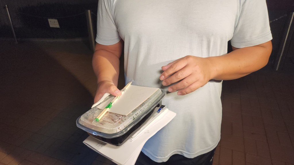 曾男手持入境處提供的飯盒，離開總部後即場開餐。黎志偉攝