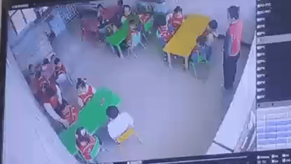 闭路电视画面显示，左边靠墙一名女幼师走到一名幼童身后拉扯他的衣服。