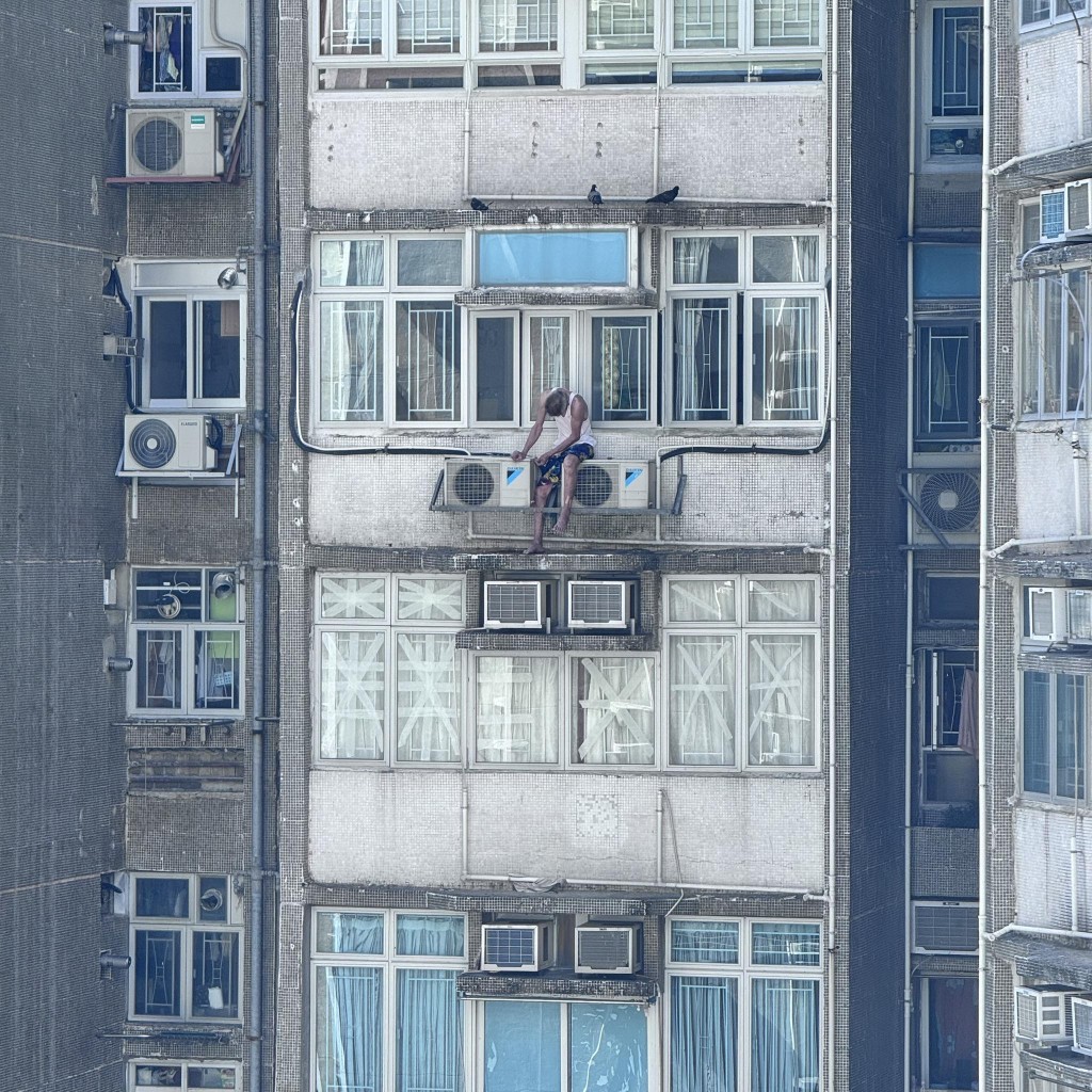 一名身穿白色背心的老翁爬出窗外維修冷氣機。fb「柴灣人柴灣事」Chan Hon Fai攝