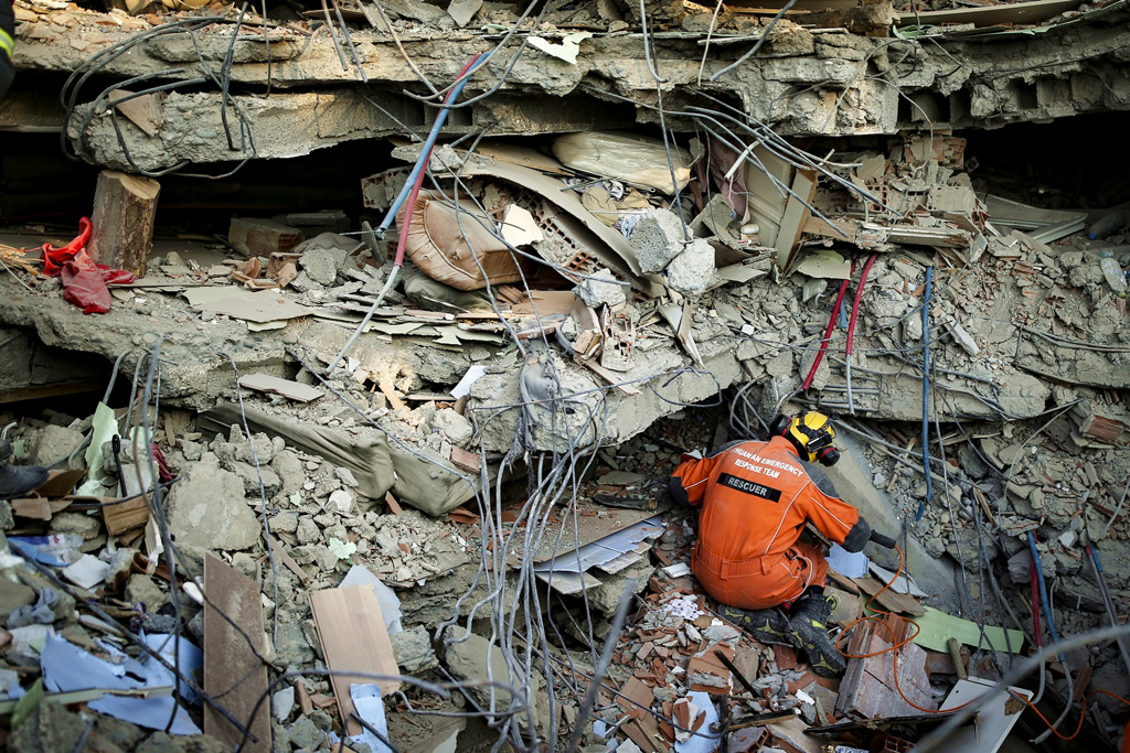 救难人员在高耸的瓦砾堆下救灾。 美联社