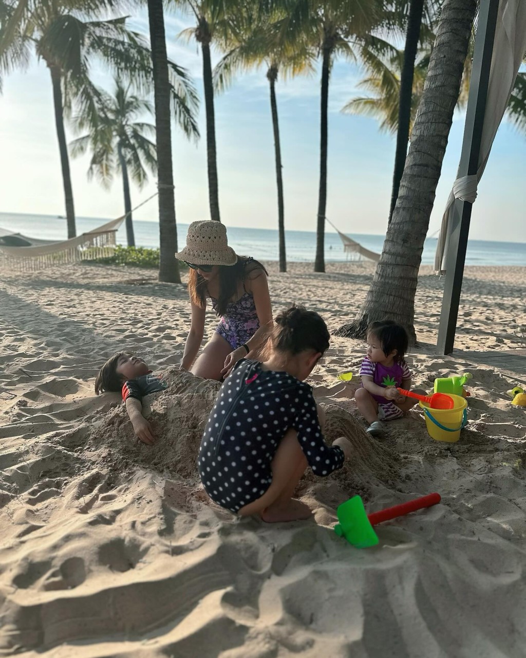 鍾嘉欣跟7歲大女Kelly（前左）和1歲細女Anika（前右）合力把5歲兒子Jared（後左）身軀埋在沙堆，Jared則一臉享受，相當搞笑。