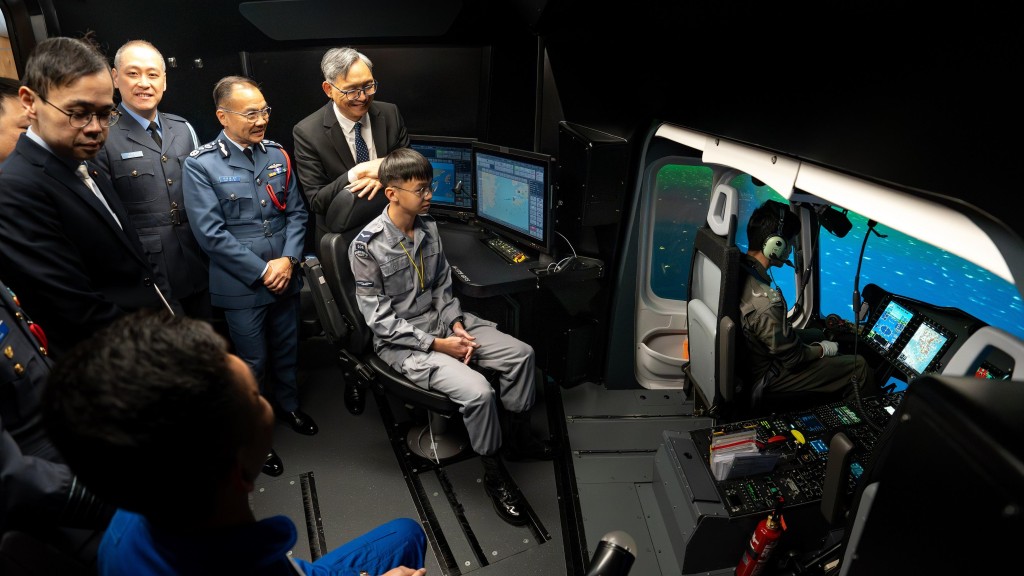 卓孝業（左四）於直升機模擬飛行器與航青團團員交流，了解其學習成果。政府新聞處