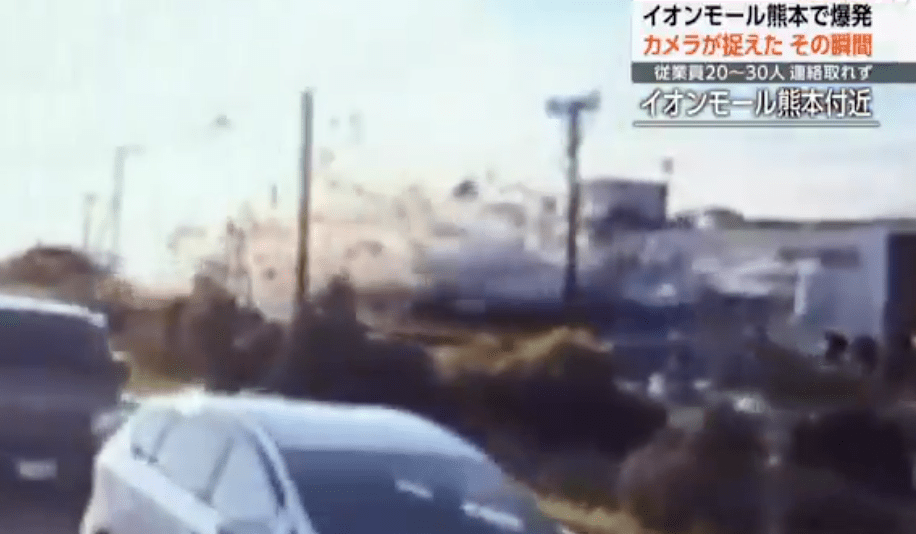 画面右侧的商场建筑突然发生爆炸，一团浓厚的白色烟雾瞬间喷涌而出。