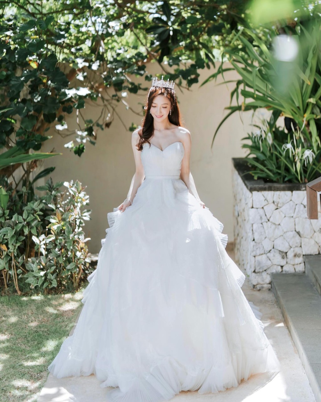 婚礼进场时，何依婷换上本地著名设计师Kev Yiu的纯白露肩婚纱，拖尾裙摆以多层法国喱士营造出浪漫轻盈感，加上闪烁皇冠造型，犹如公主般。