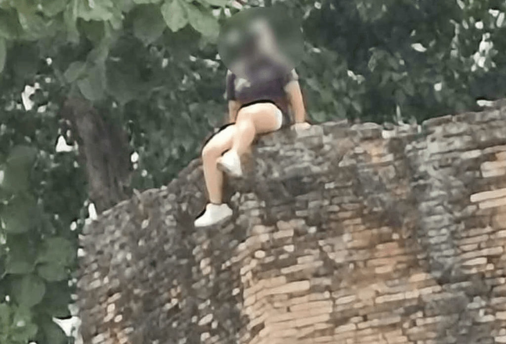 攀爬至當地富有歷史意義的古城牆上坐著拍照,甚至將雙腿懸掛在城牆外,引來當地民眾不滿。星洲網截圖 攀爬至當地富有歷史意義的古城牆上坐著拍照,甚至將雙腿懸掛在城牆外,引來當地民眾不滿。星洲網截圖