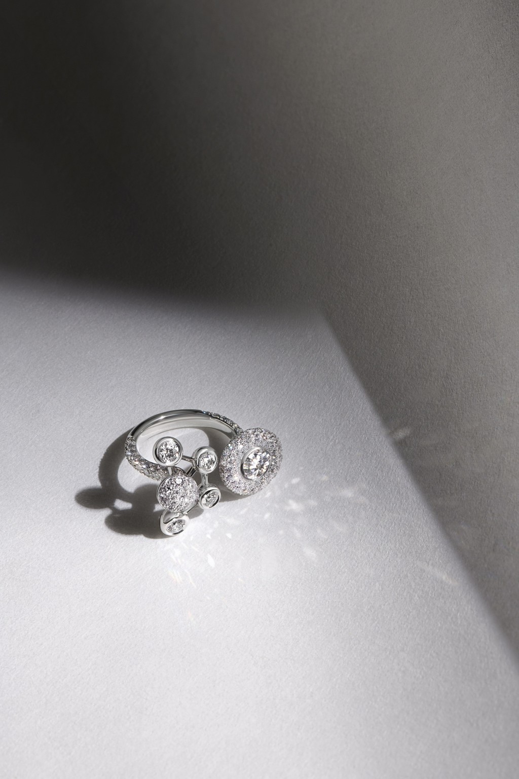 Atomique白金鑽石指間戒/$322,000，採用開放式設計，呈現兩個對比鮮明的圖案，包括單顆重0.69卡圓形明亮式鑽石，以密鋪鑲鑽石圍繞，另一個是四顆彼此鉸接鑲嵌的鑽石，宛如衞星般飄浮在中央的密鋪鑲鑽石拱形圓頂的周圍。