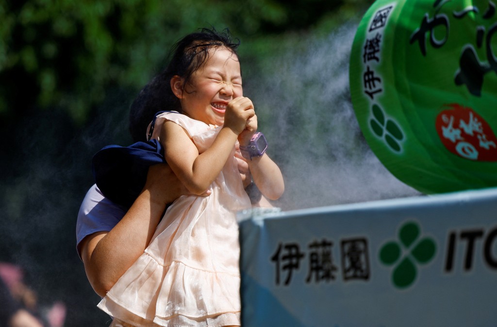 小女孩抵受不住酷熱，要以室外設置的噴灑涼霧消暑。路透社