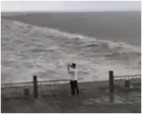 浙江海寧一名男子於錢塘江海塘邊拍潮水。影片截圖