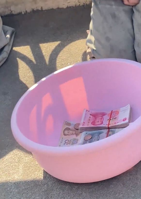 男乞讨面前的盘子放有大量现金。影片截图