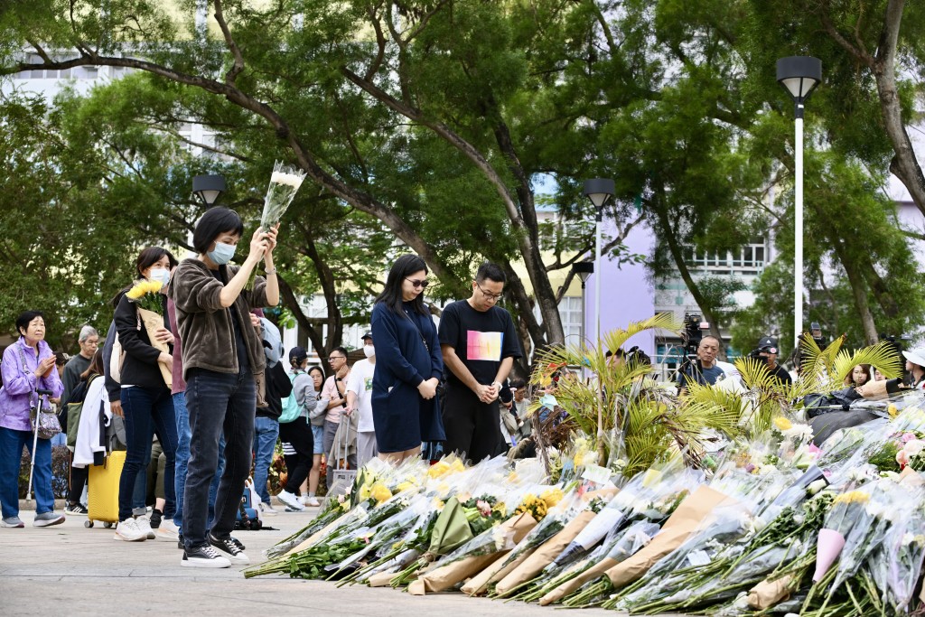 地上除擺放大量鮮花，亦有毛公仔、水果、零食及飲品等祭品