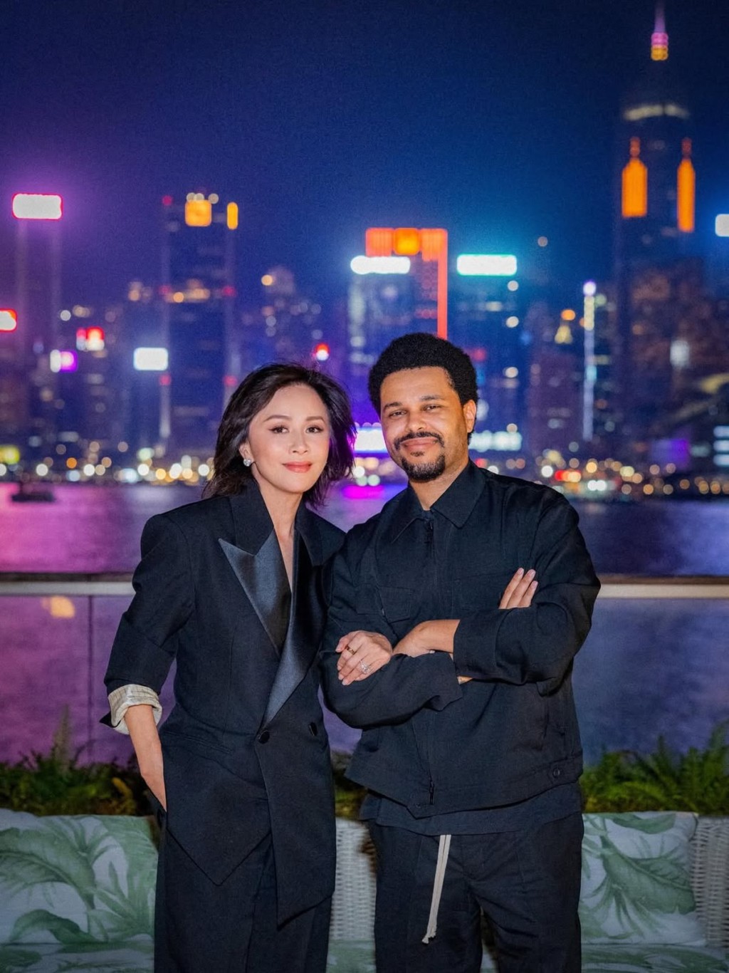劉嘉玲一身俐落黑色西裝與 The Weeknd 並肩合照，背後維港璀璨夜景格外搶眼。