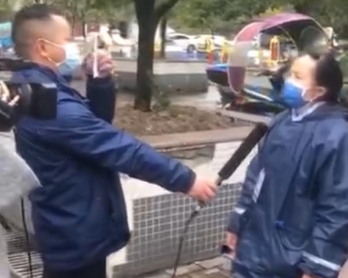 視頻中的女社區工作人員接受採訪時，有工作員拿著疑似採訪稿給她照讀。網圖