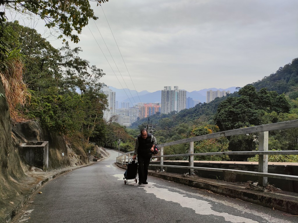68岁村长戴辛有买餸返回黄竹洋村时，亦要徒步半小时手拉买餸车爬坡返村。(莫家文摄)