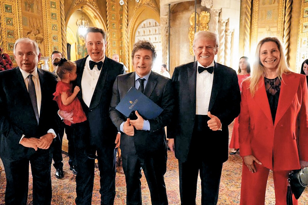 馬斯克抱着一個小女孩，周四在佛州海湖莊園與特朗普、阿根廷總統米萊（中）合照。從左到右是阿根廷外交部長沃特因、馬斯克、米萊、特朗普、米萊的妹妹卡琳娜。