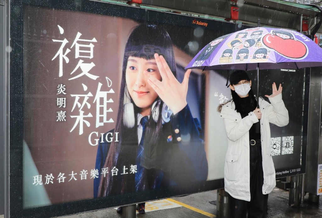 Gigi拿着有自己卡通公仔雨傘在燈箱前打卡。