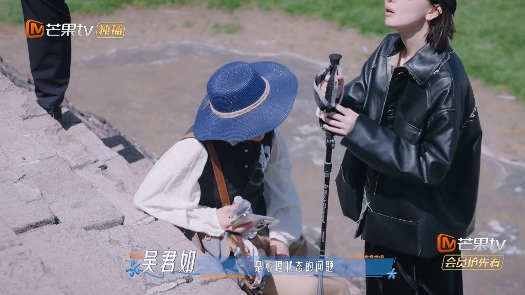 吳君如行至中途已顯疲態，手持水樽坐於石階旁稍作歇息，周冬雨則手持登山杖在側照應。