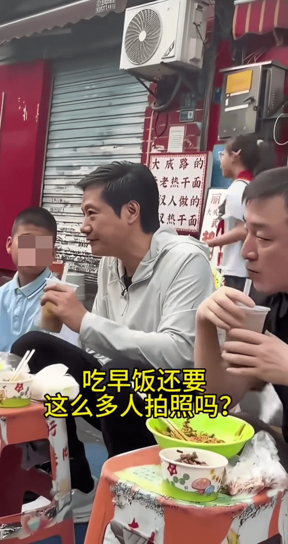 雷军武汉街头吃早餐，正与身边的小男孩聊天时，身后路过一名小女孩。