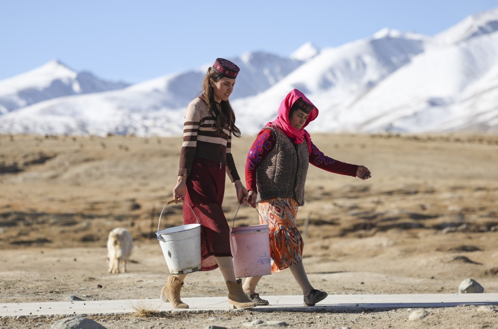 在新疆塔什库尔干塔吉克自治县瓦恰乡夏布孜喀拉村，艾尔开牙·多力开（左）帮母亲拎水。 新华社