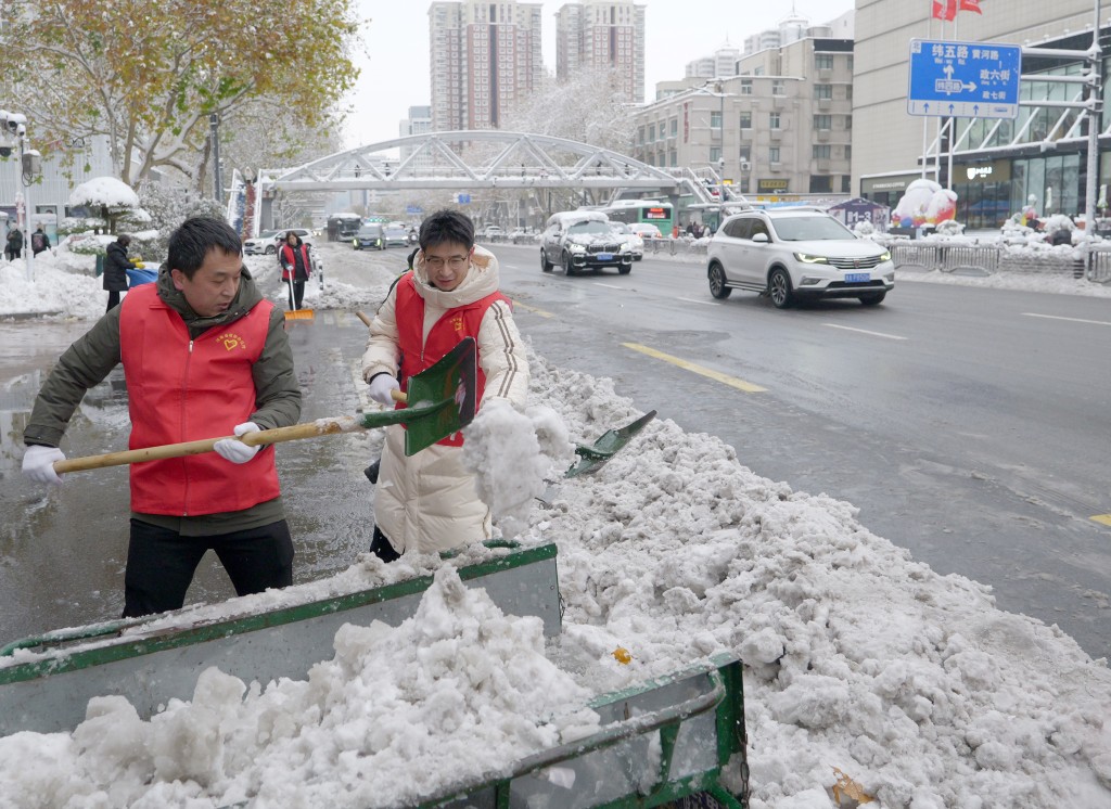 12月11日，在郑州市花园路上，志愿者清除道路积雪。 新华社