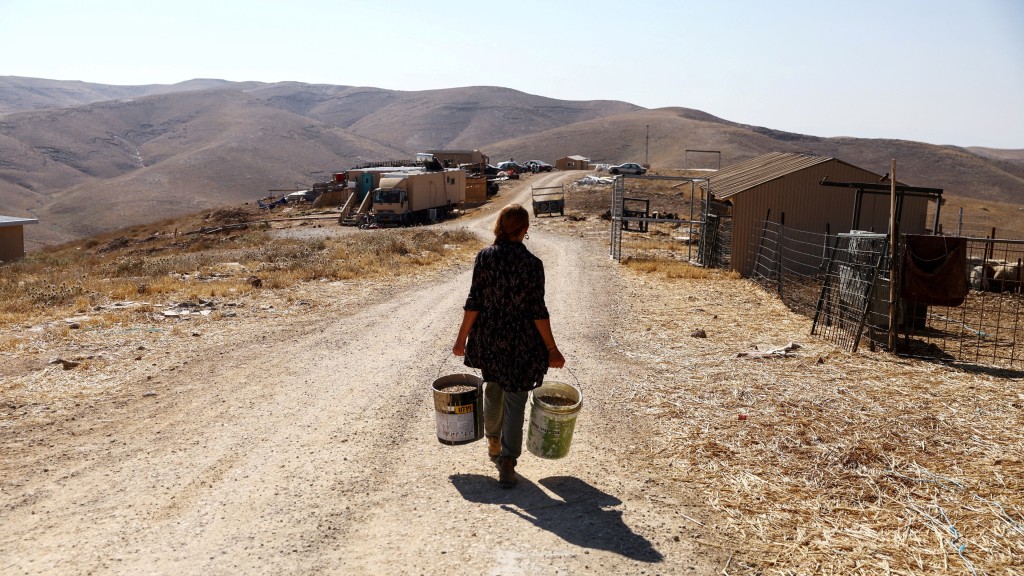 一名定居者在约旦河西岸犹太定居点凯达尔（Kedar）附近的凯达尔羊农场提着水桶。 路透社