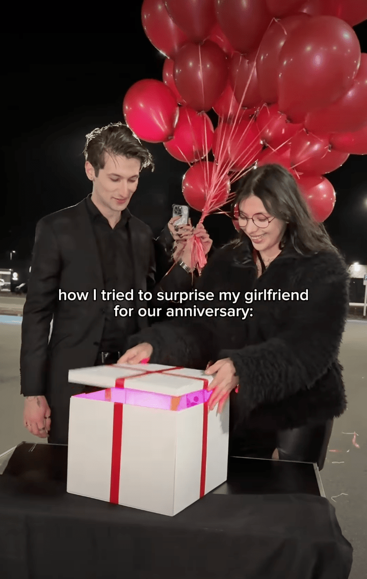 片中可見，一對情侶站在擺放禮盒的桌旁，男方身穿黑色西裝，女方手持紅色氣球。桌上是一個繫有紅絲帶的白色大禮盒，內裡更設有粉紅色燈光營造氣氛。