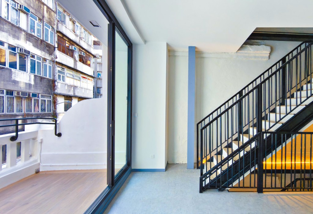 经修复的长窄木楼梯，墙面原有的砖砌结构得以保留，仅施以一层粗糙质感的油漆覆盖，而最注目的是宽阔的骑楼。