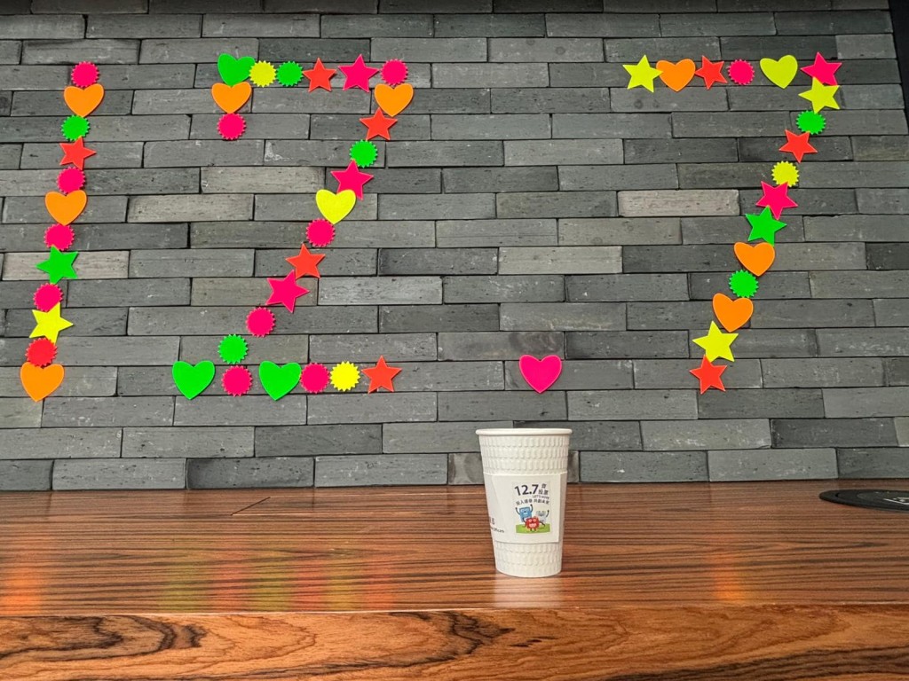 咖啡杯杯套貼上「票箱家族」的貼紙，牆上還拼有「12.7」的數字，呼籲大家12月7日齊投票。何永賢fb