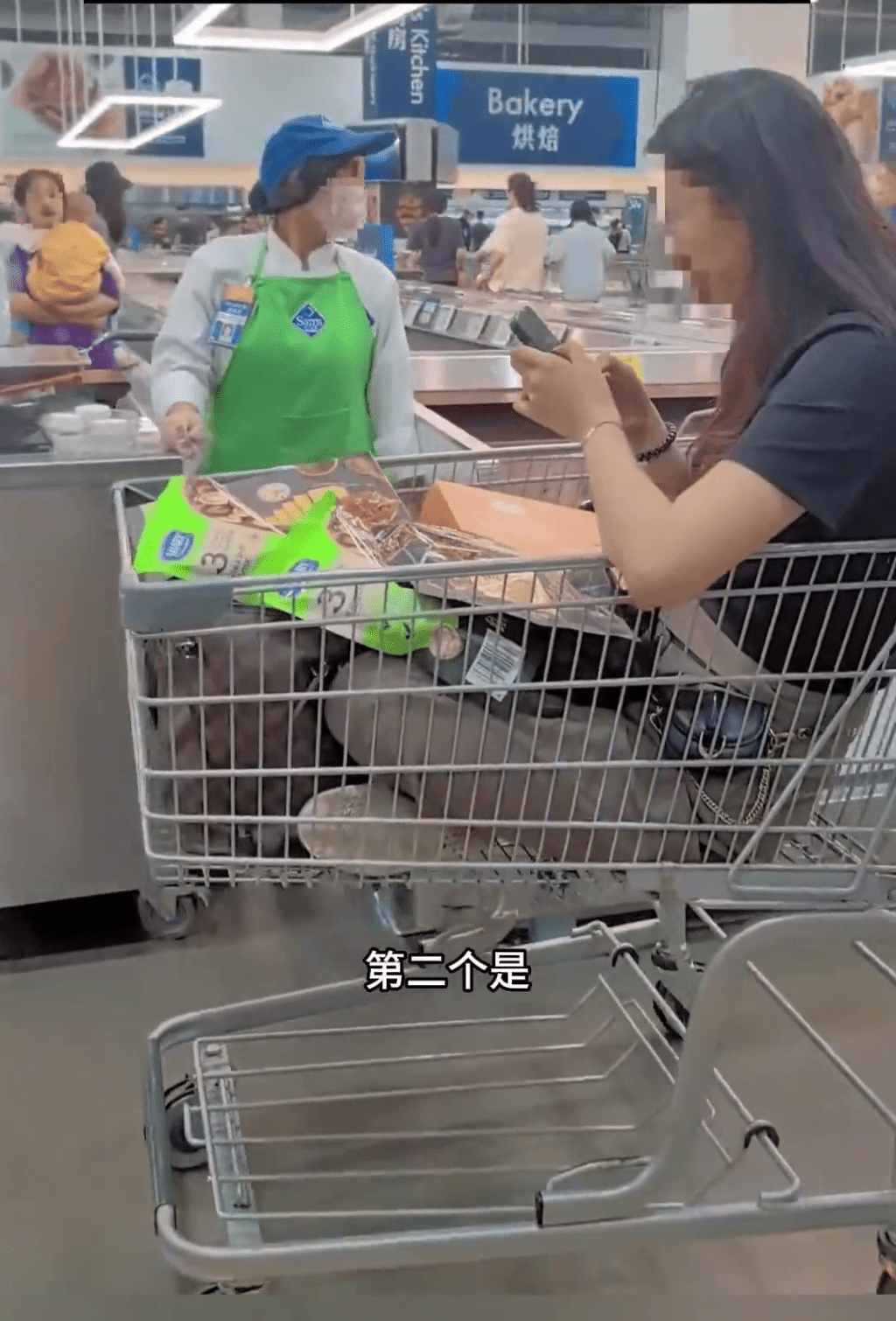 一名黑衫女子坐在购物车在玩手机，身上还有选购的物品。