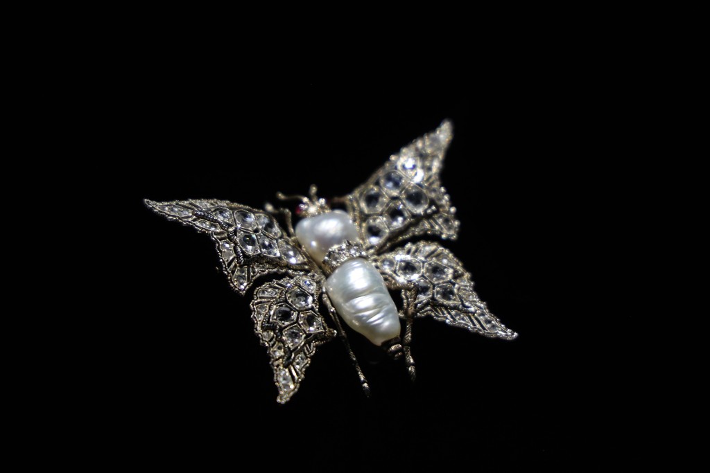 这枚蝴蝶胸针出自品牌创始人Mario之手，属于1950年代设计风格，以白金镶嵌2颗巴洛克珍珠、2颗圆形蛋面切割红宝石及76颗玫瑰式切割钻石。。