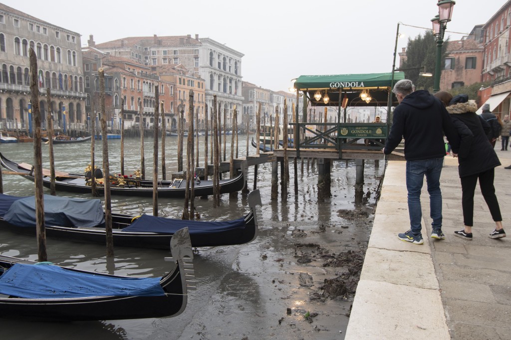 意大利威尼斯的退潮期間，人們看著停靠在運河沿岸的「貢多拉」。AP