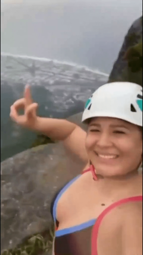 女游客在悬崖边摆出手势自拍。 网片截图