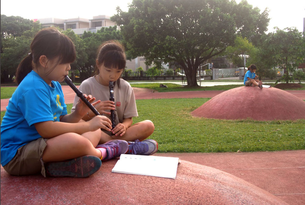 有學生坐在小圓丘練習吹直笛。高雄市政府網
