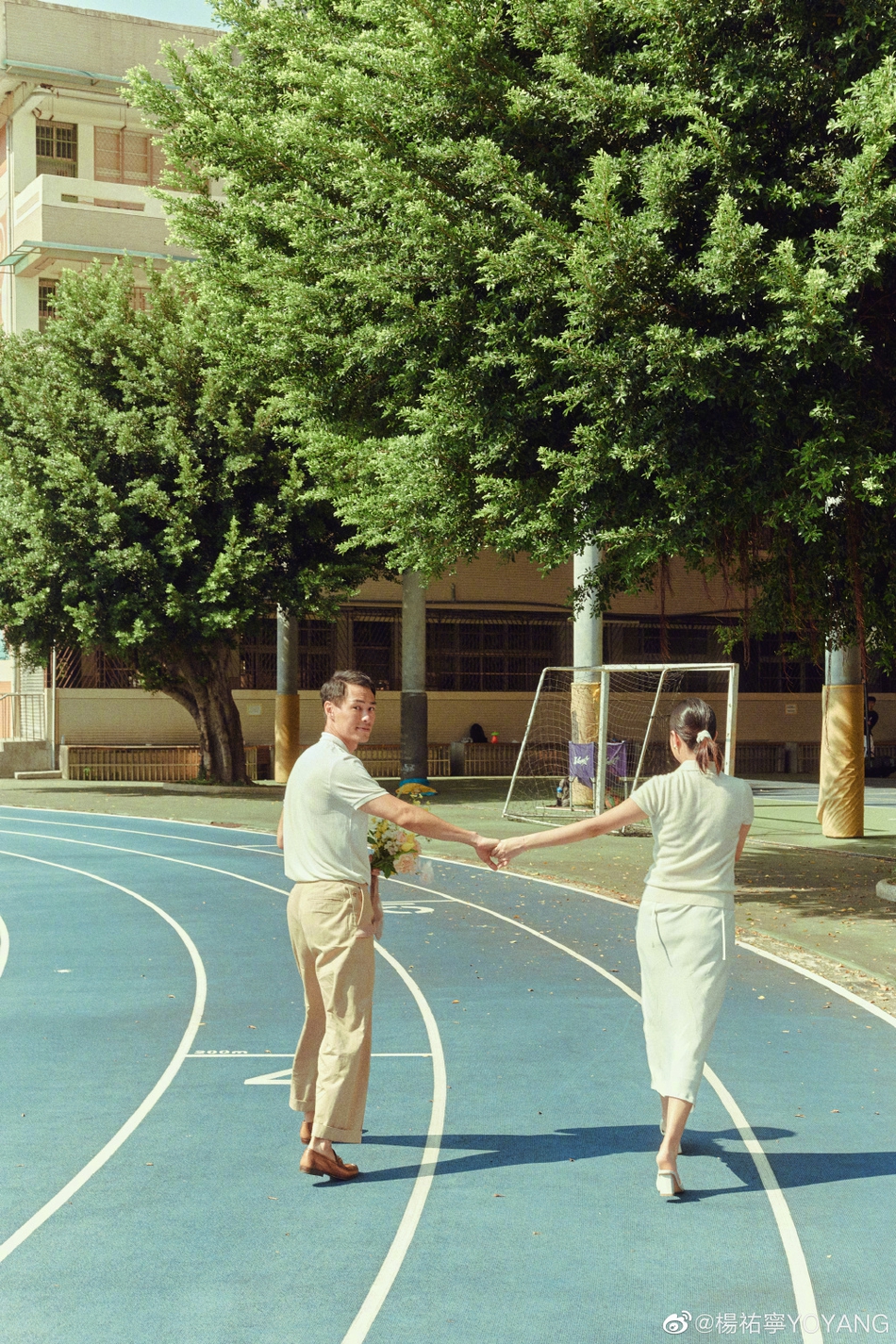 二人手拖手於運動場跑道上漫步。