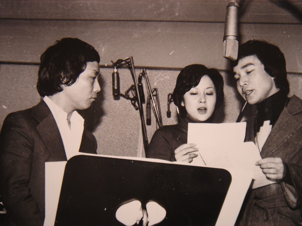 1976年電影《愛在夏威夷》中，由謝雷(右)與該片女主角甄珍(中)合唱主題曲，顧嘉煇(左)則在場監督。