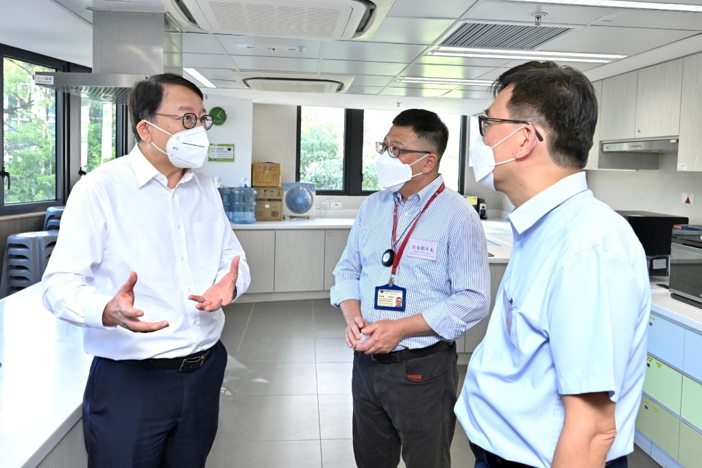 政务司司长陈国基（左一）到访明爱荃湾社区中心，听取香港明爱的代表介绍中心向基层家庭提供的不同设施和服务。他们身处该中心的烹饪室。